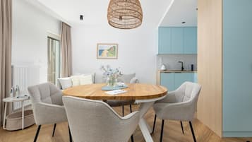 A modern dining area with a round wooden table, grey upholstered chairs, a woven pendant light, and a kitchen with light blue cabinets in the background.