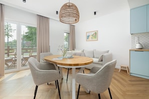 Un espace repas moderne avec une table ronde en bois, des chaises à revêtement gris et un luminaire suspendu en fibres tressées.