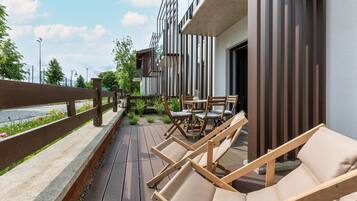 Eine Holzterrasse mit Liegestühlen und einem Tisch, mit Blick auf ein Gewässer und eine Reihe von Gebäuden.