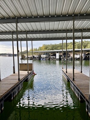 A covered dock area with wooden walkways over water, leading to a marina with boats and a building in the background. - Sleeps 20 Lodge w/ Boat Slip, Game Room & Pools, 5 Min to Silver Dollar City (Branson)