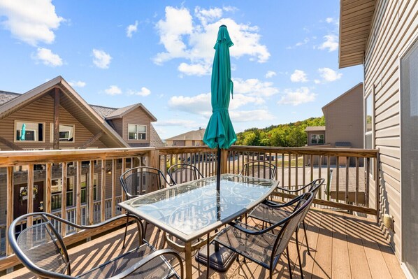 A deck with a glass table and chairs, surrounded by wooden railings, under a clear sky.