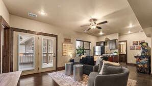 A spacious living room with a dark-colored sofa, a coffee table, and a rug. There is a ceiling fan, a kitchen area in the background, and a sliding glass door leading to a balcony. - Lakefront Sleeps 20 | Boat Slip Included | 5 Min to SDC (Branson)