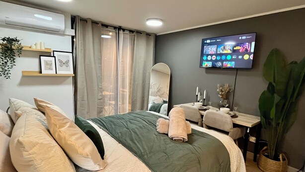 A modern hotel room with a large bed, a desk, a mirror, and a TV displaying various channels. - M&C DC 108 (Santiago)