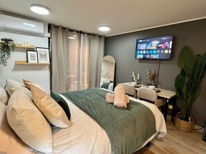 A modern hotel room with a large bed, a desk, a mirror, and a TV displaying various channels. - M&C DC 108 (Santiago)