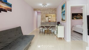 A modern living room with a grey sofa, a dining area with a table and chairs, a kitchen with a microwave and a refrigerator, and a bedroom with a bed. - Apt Close to the Beach in Canasvieiras Rfs205 (Florianópolis)