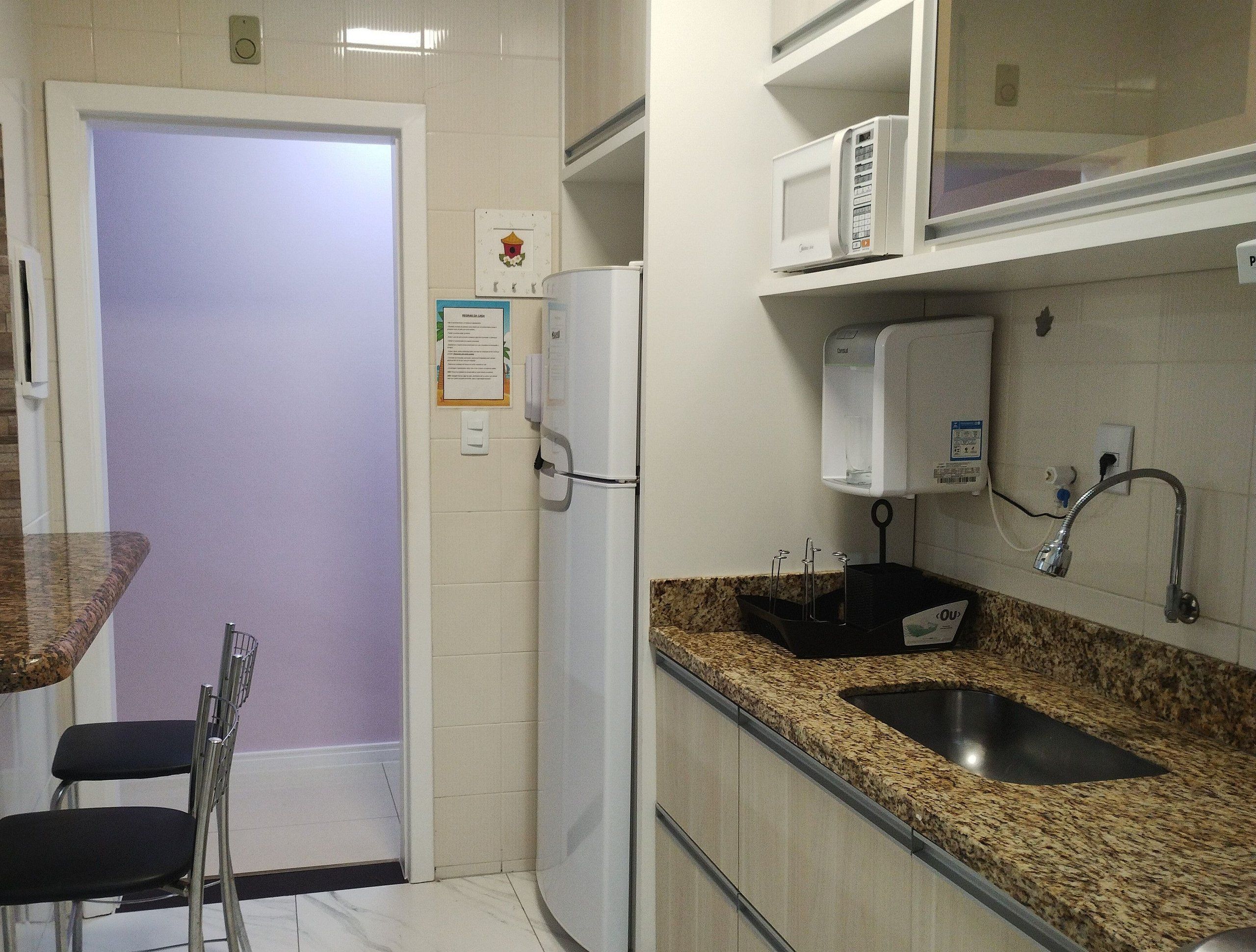 A compact kitchen with a refrigerator, microwave, sink, and a small dining area with chairs.