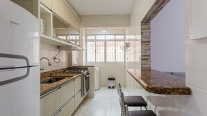 A compact kitchen with a refrigerator, stove, and sink. There is a window with bars and a trash bin. - Apt Close to the Beach in Canasvieiras Rfs205 (Florianópolis)