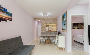 Ein modernes Wohnzimmer mit grauem Sofa, ein Essbereich mit Tisch und Stühlen, eine Küche mit Mikrowelle und Kühlschrank sowie ein Schlafzimmer mit Bett.
