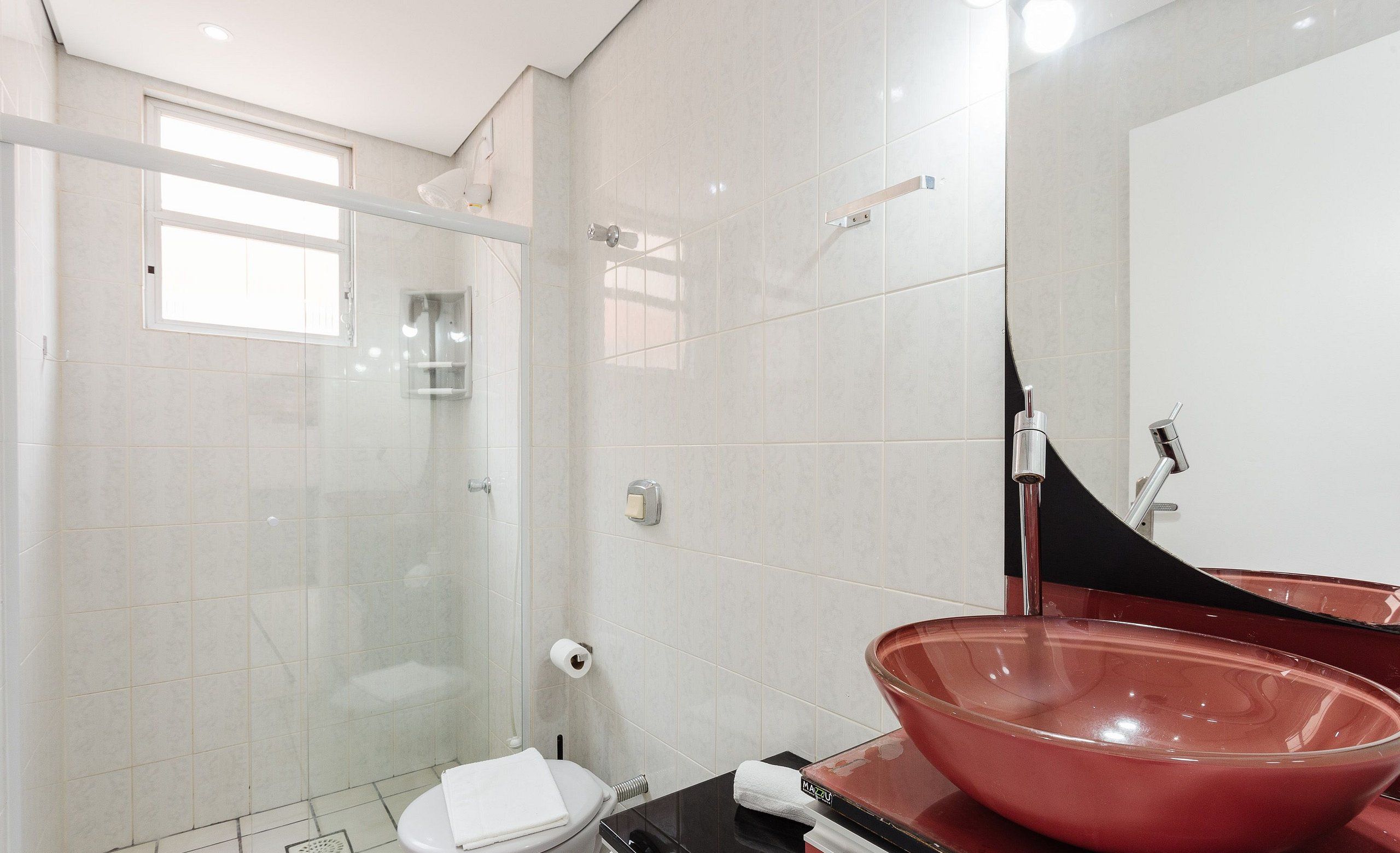 A modern bathroom with a glass shower enclosure, a white toilet, and a red vessel sink.