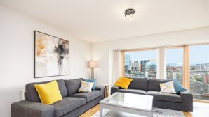 Ein modernes Wohnzimmer mit zwei grauen Sofas, einem weißen Couchtisch und einem großen Fenster mit Blick auf die Stadt.