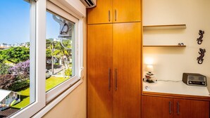 A room with a large window, wooden wardrobe, and a small table with a lamp and radio. - Apart W/barbecue 10min From Jurere Beach Rf203 (Florianópolis)
