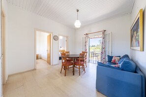 Une pièce comprenant une table à manger, des chaises, un canapé, un luminaire au plafond et une fenêtre avec des rideaux.