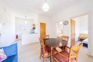 Une pièce comprenant une table à manger, des chaises, un lit, une table de chevet, une horloge et un coin cuisine.