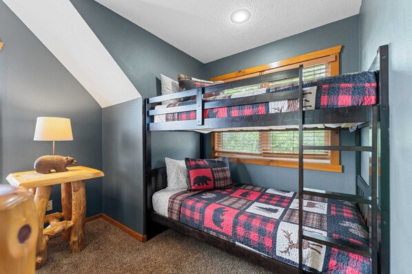 A bunk bed room with a wooden desk and a lamp.