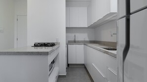 A compact kitchen with white cabinetry, a built-in oven, a gas stove, and a stainless steel refrigerator. - Apt w/ BBQ 300m From the Beach in Floripa Res201 (Florianópolis)