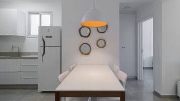 Una cocina moderna con un refrigerador blanco, una mesa de comedor con sillas y una lámpara colgante.