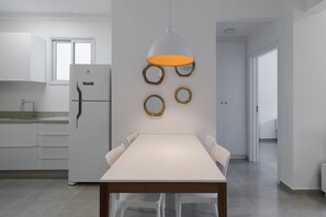 Una cocina moderna con un refrigerador blanco, una mesa de comedor con sillas y una lámpara colgante.