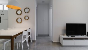 A modern dining area with a white table, chairs, and a pendant light. A white cabinet with a flat-screen TV is visible. - Apt w/ BBQ 300m From the Beach in Floripa Res201 (Florianópolis)