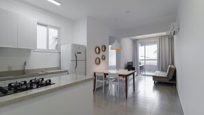 A modern kitchen with a central island, a dining area with a table and chairs, and a living space with a sofa and a TV. - Apt w/ BBQ 300m From the Beach in Floripa Res201 (Florianópolis)