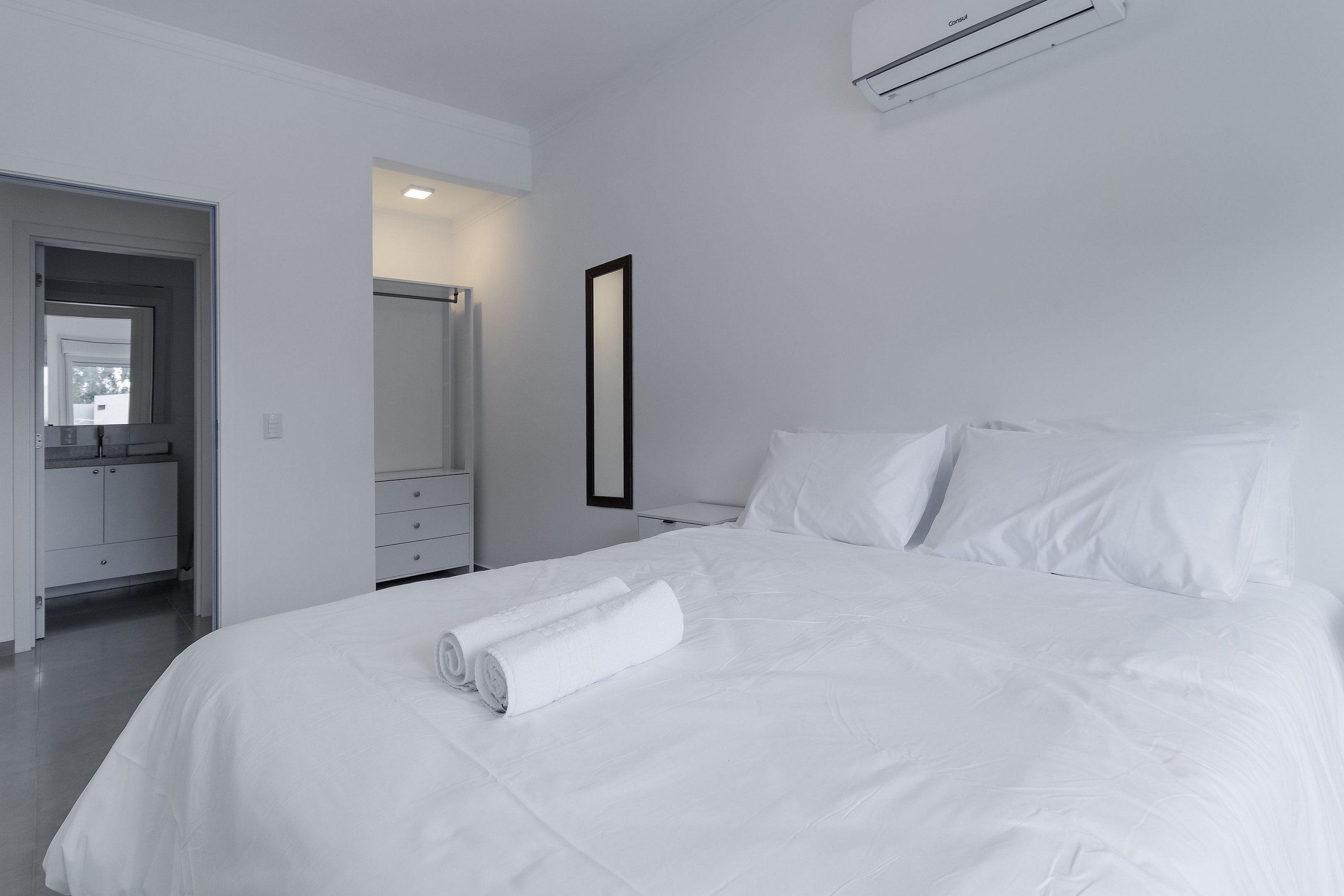 Una habitación de hotel moderna con una cama bien hecha, un baño con espejo y una paleta de colores blancos.