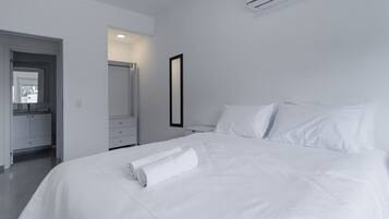 Una habitación de hotel moderna con una cama bien hecha, un baño con espejo y una paleta de colores blancos.