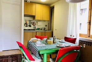 Une cuisine compacte avec des meubles en bois, une table à manger recouverte d’une nappe à carreaux et des chaises rouges.