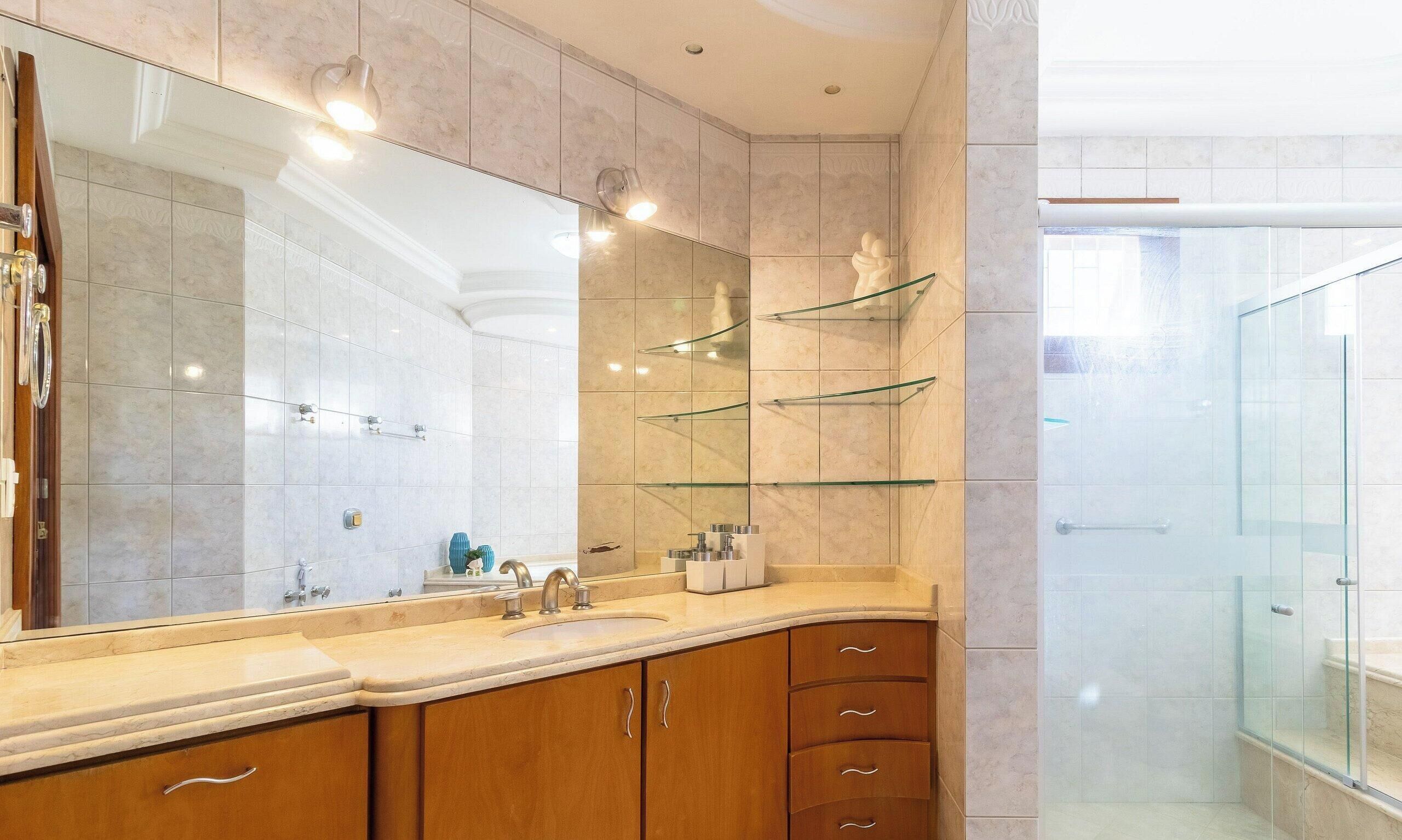 A modern bathroom with a large mirror, wooden cabinets, and a glass shower enclosure.