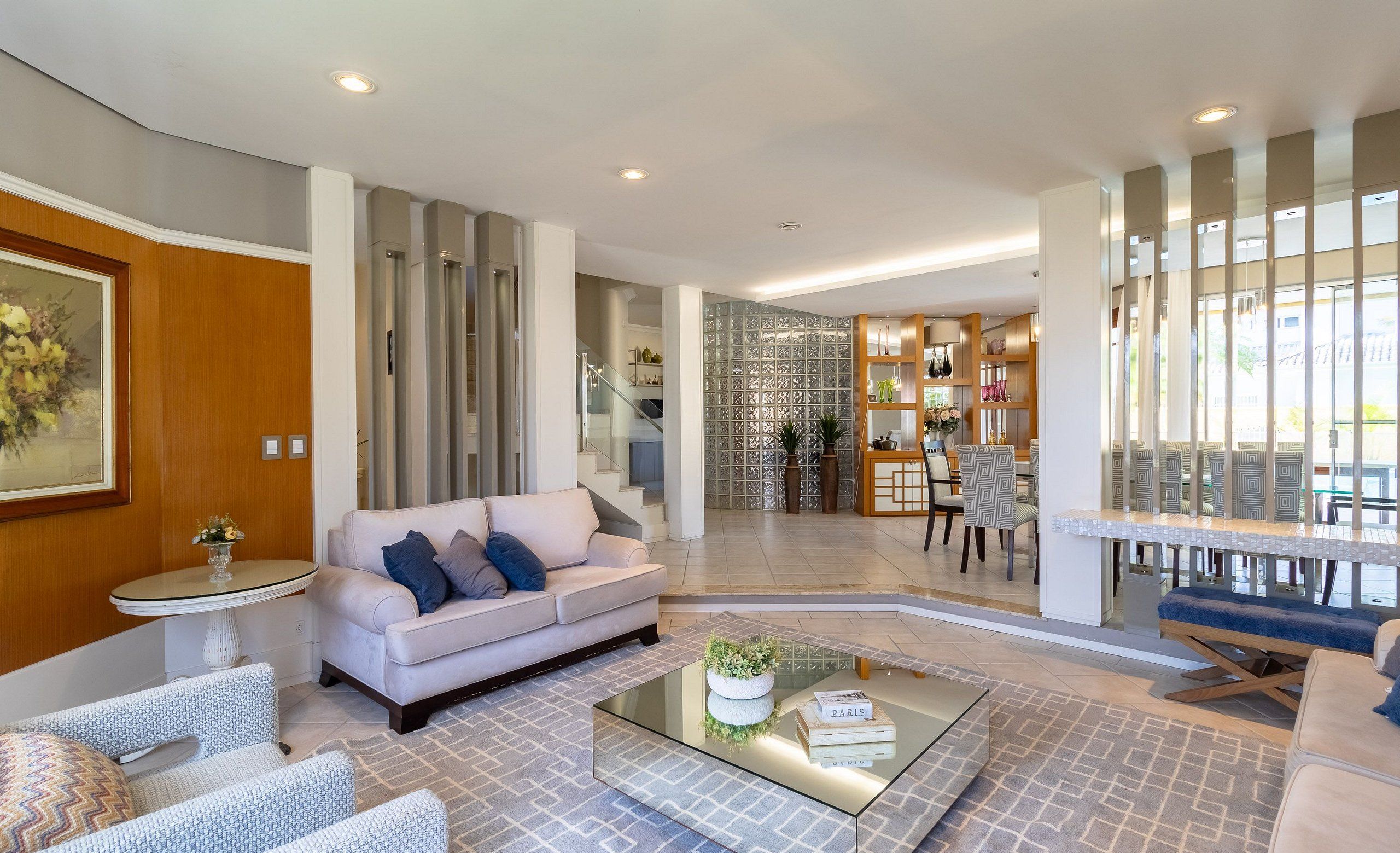 A modern living room with a sofa, armchairs, a coffee table, and a dining area with a table and chairs.