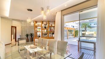 A modern living room with a glass dining table, patterned sofas, and a large window with a view of the outside.