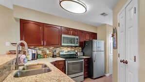 A kitchen with wooden cabinets, a stainless steel sink, a microwave, a refrigerator, and a stove. - Waterway Village - 13H (Myrtle Beach)