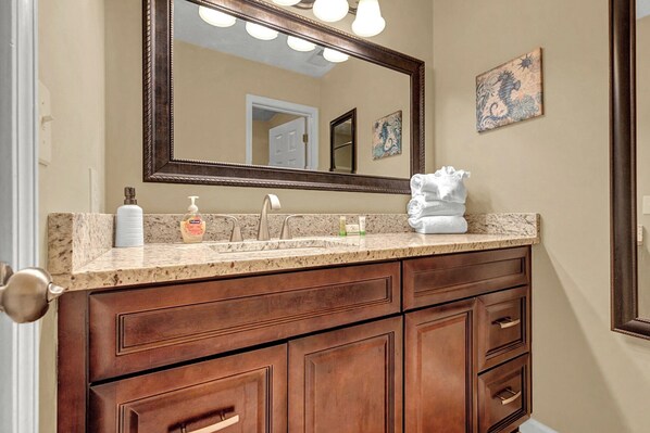 A bathroom with a marble countertop, a large mirror, and wooden cabinets. - Waterway Village - 13H (Myrtle Beach)