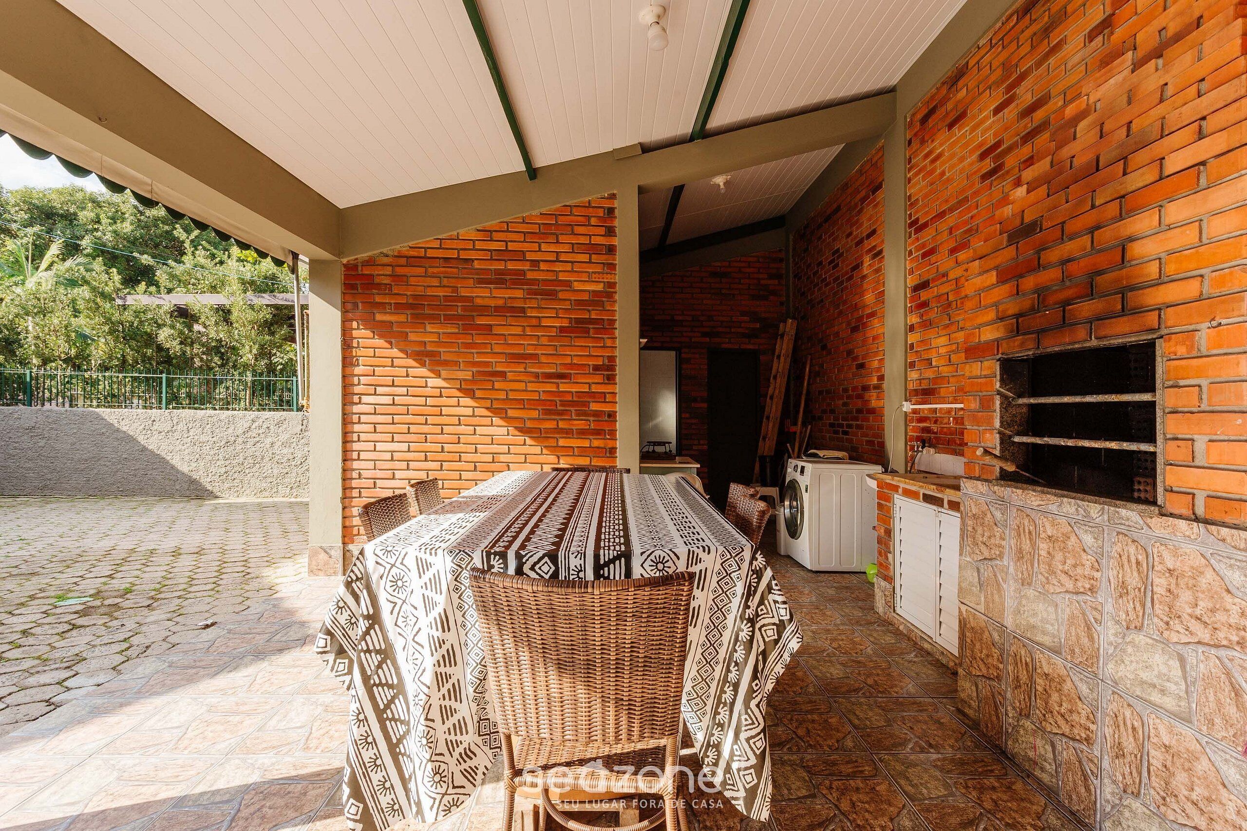 Un patio exterior con pared de ladrillo, una mesa cubierta con sillas y una lavadora.