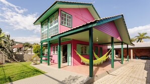 A two-story house with a pink and green exterior, a covered porch with a hammock, and a brick pathway leading to the entrance. - Pleasant Townhouse w/ BBQ 90m From the Sea Rdd657 (Florianópolis)
