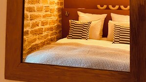 A bedroom with a stone wall, a round light fixture, and a bed with striped pillows. - Jas Tihou bergerie premium swimming pool Provence (Le Beausset)