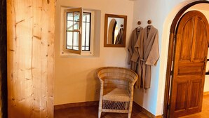 A room with a wooden wardrobe, a wicker chair, a mirror, and a wooden door. - Jas Tihou bergerie premium swimming pool Provence (Le Beausset)