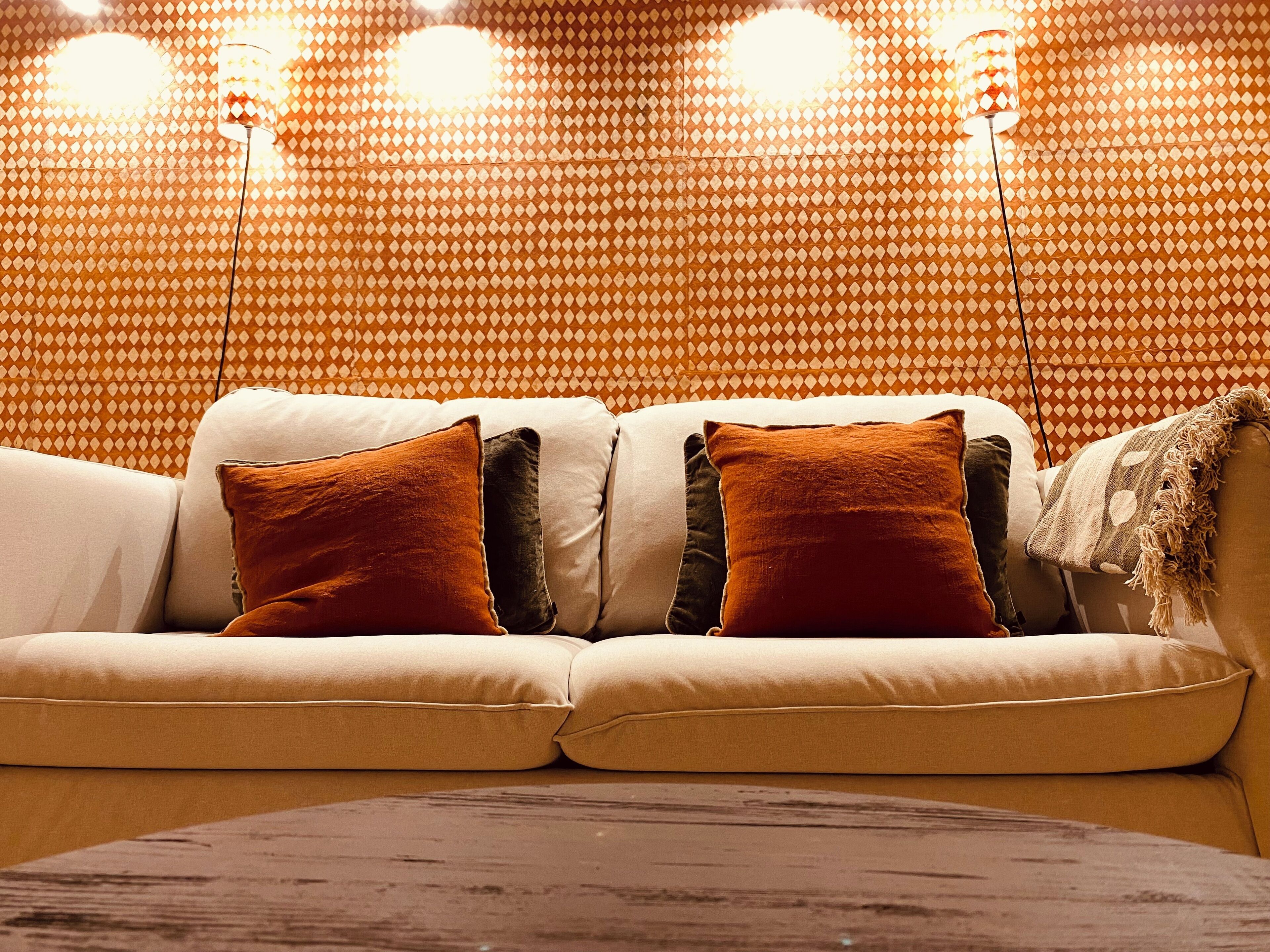 A sofa with multiple cushions in a room with patterned wallpaper and a floor lamp.