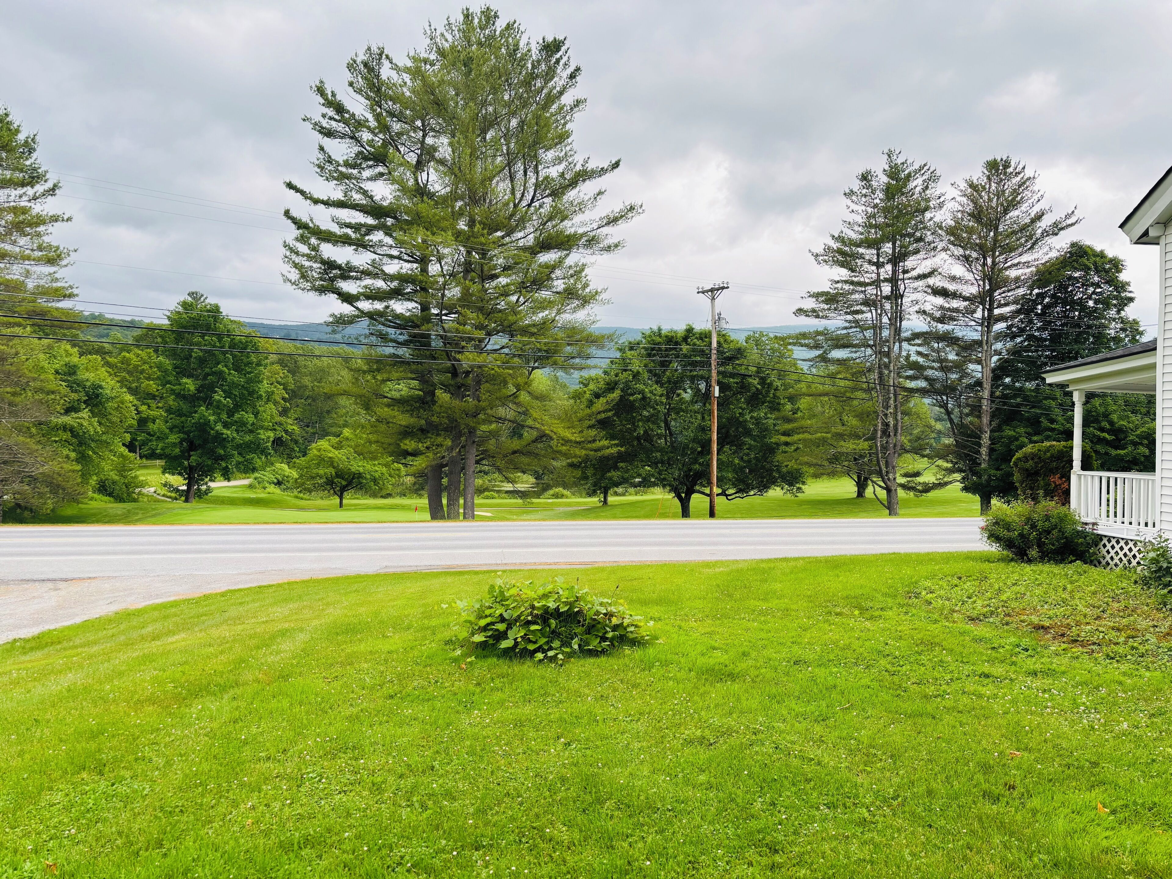 A residential area with a well-maintained lawn, a house with a porch, and a road leading to a body of water.