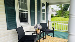 A porch with two black chairs and a small table, a yellow patterned rug, and a vase of flowers.
