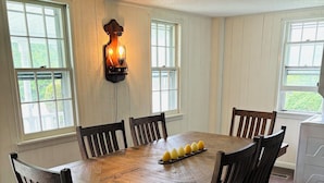 A dining area with a wooden table, six chairs, a patterned rug, and a wall-mounted light fixture.