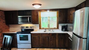 A kitchen with dark wooden cabinets, stainless steel appliances, a window with blinds, and a wooden floor.