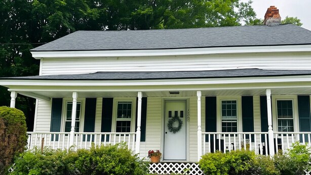 A two-story white house with a front porch, a door with a wreath, and a chimney.
