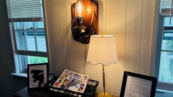 Una habitación con una lámpara de pared, una mesa con lámpara, una cesta de revistas y un cartel de bienvenida.