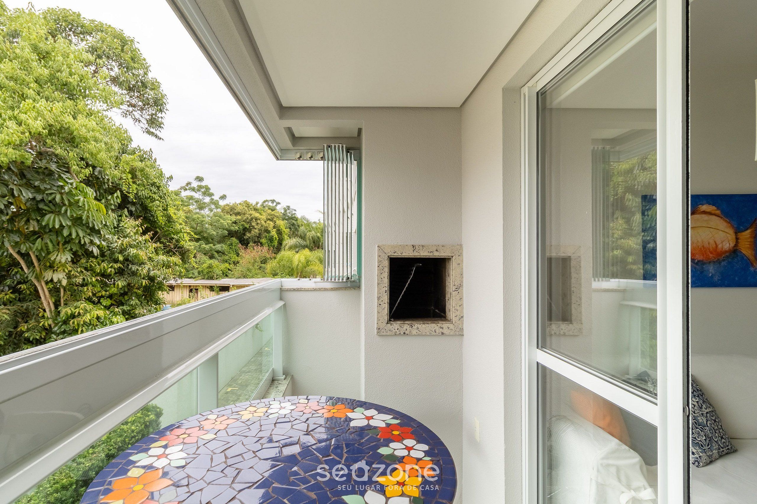 Ein Balkon mit gefliestem Boden, Glasgeländer und Blick auf Grünflächen.