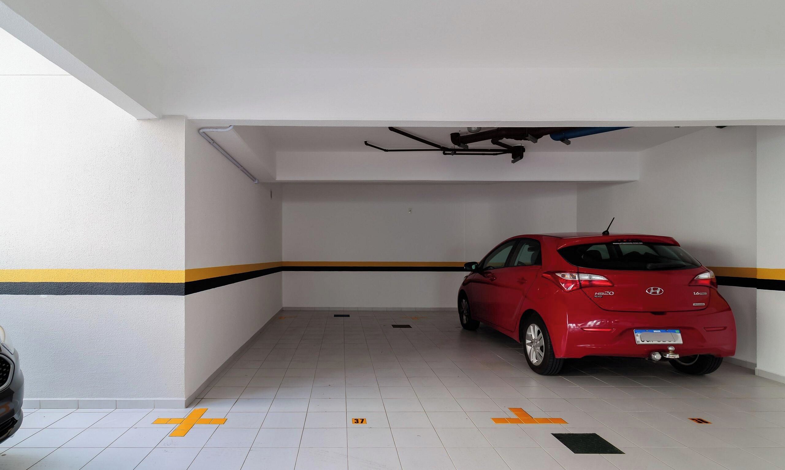A parking garage with a red car parked in a space marked with a yellow cross.