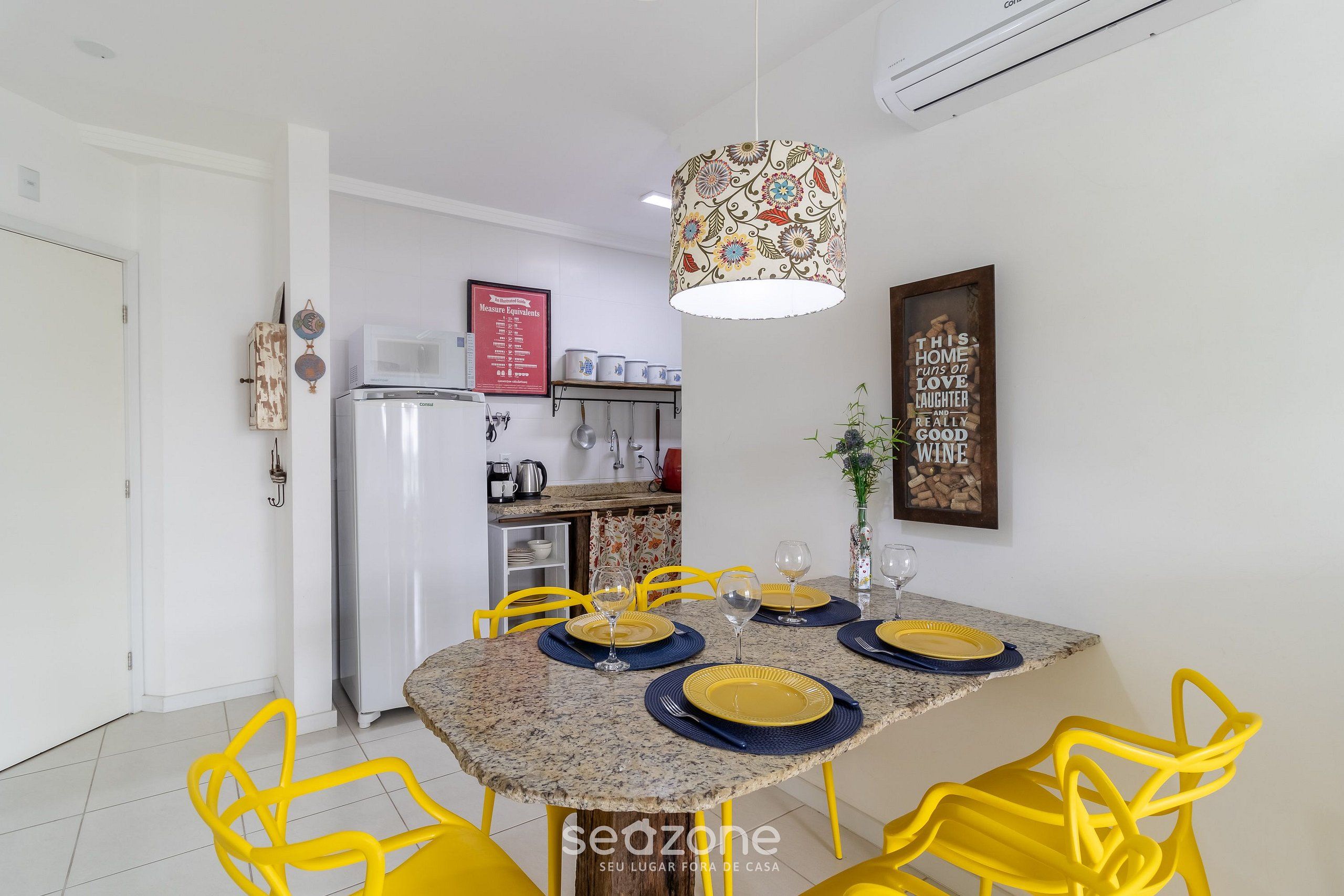 A dining area with a granite table, yellow chairs, and a patterned pendant light.
