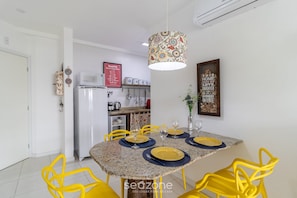 A dining area with a granite table, yellow chairs, and a patterned pendant light. - Moderno Apto c/ Piscina em Canasvieiras RCP202 (Florianópolis)