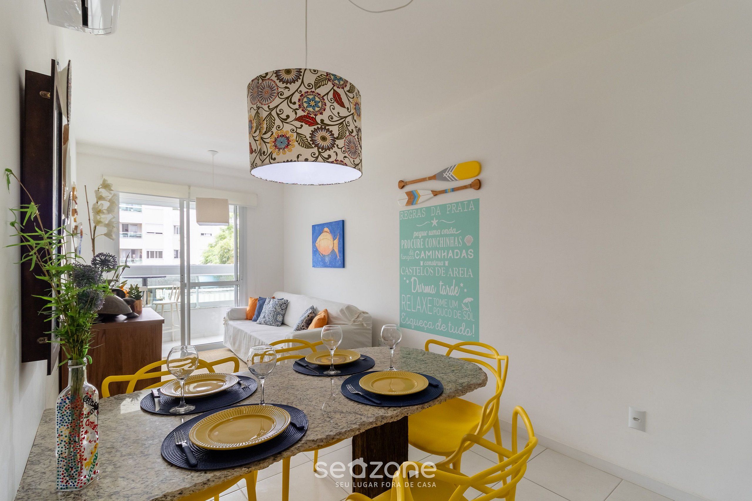 A dining area with a table set for four, yellow chairs, a decorative lamp, and a view of the outside.