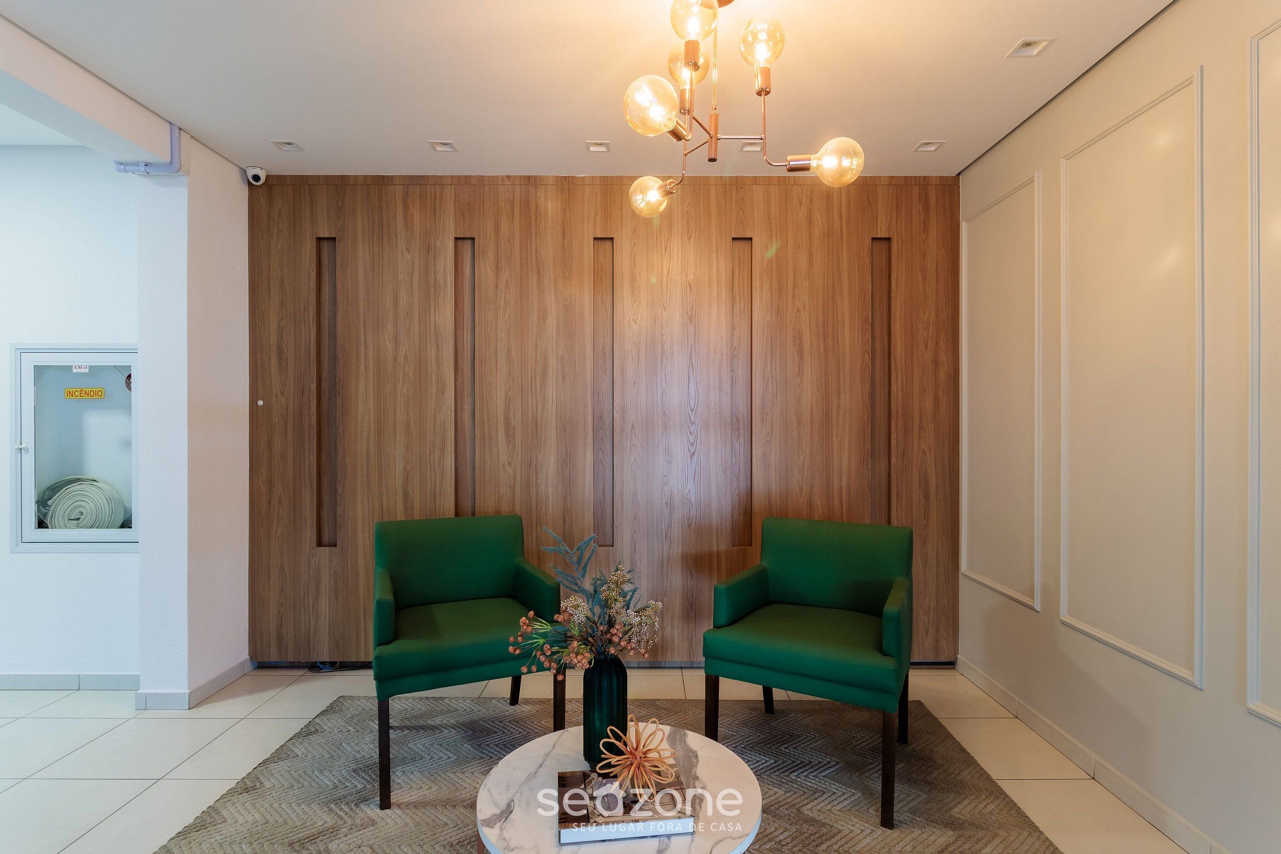 Un vestíbulo moderno con dos sillones verdes, una mesa de centro de mármol con un jarrón y un revestimiento de pared de madera.
