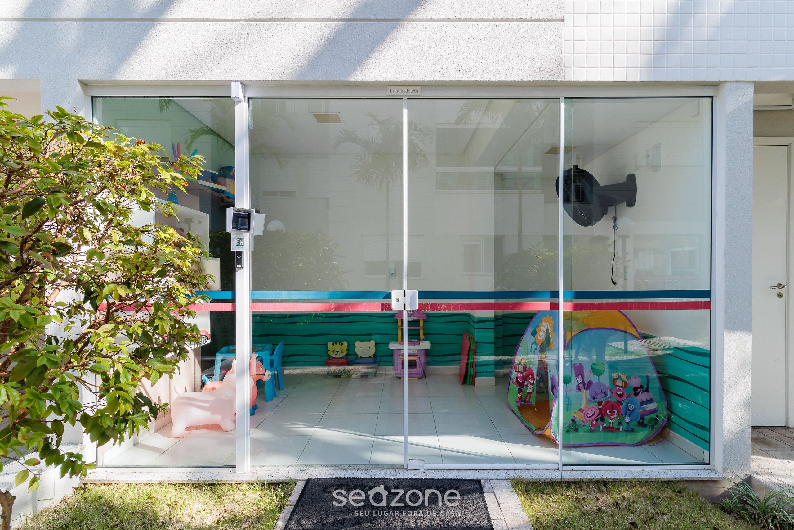 A glass-fronted entrance with a children's play area visible inside, a doorbell, and a sign reading 'seozone'.