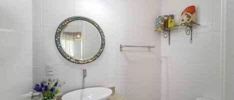 A bathroom with a round mirror, a white sink, a towel rack, and a shelf with decorative items.